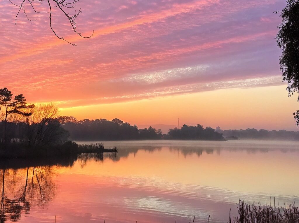 Nascer do sol sereno sobre um lago calmo com cores pastéis suaves, simbolizando uma manhã de terça-feira tranquila em 21 de janeiro de 2025.